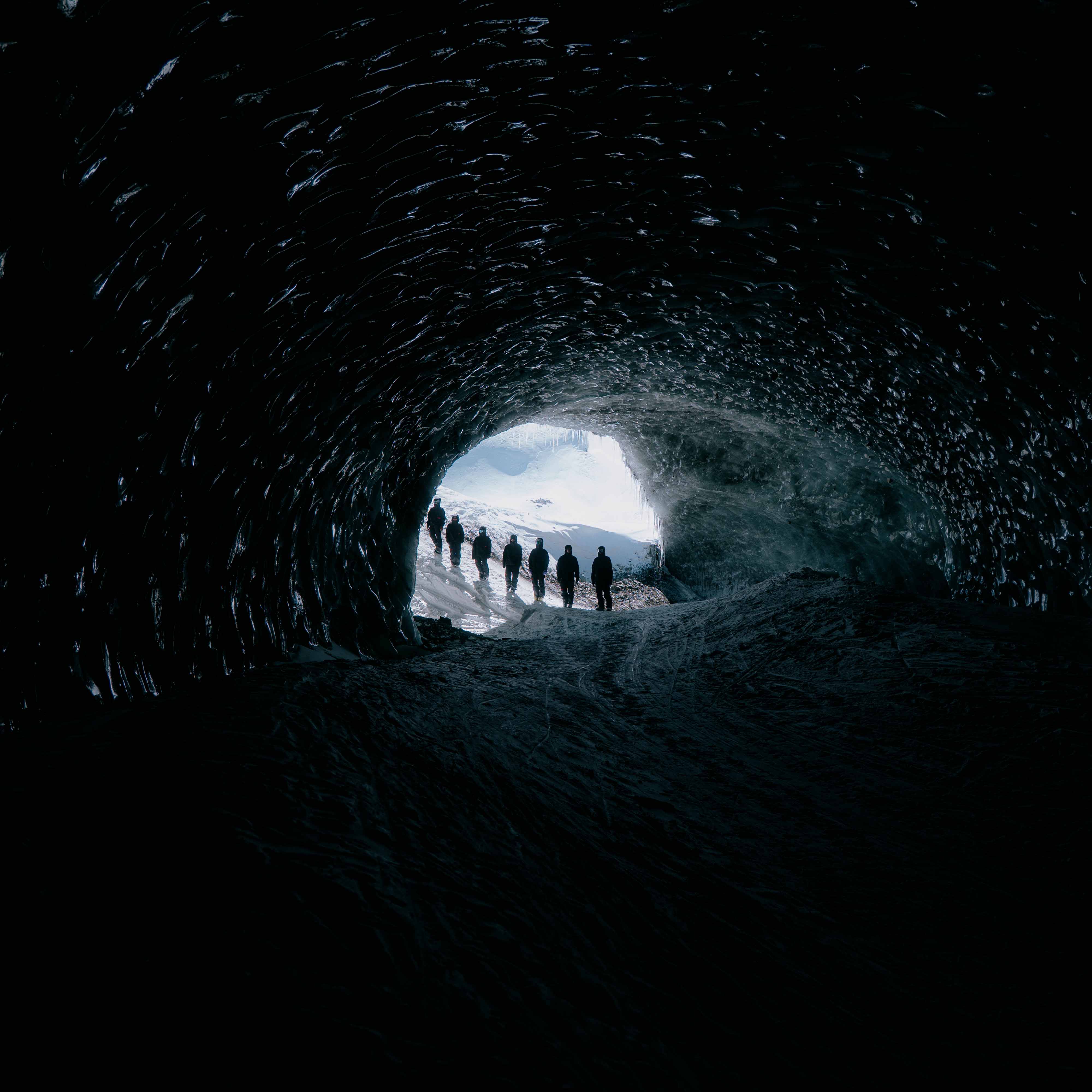 People walking through a dark ice cave towards a bright opening.