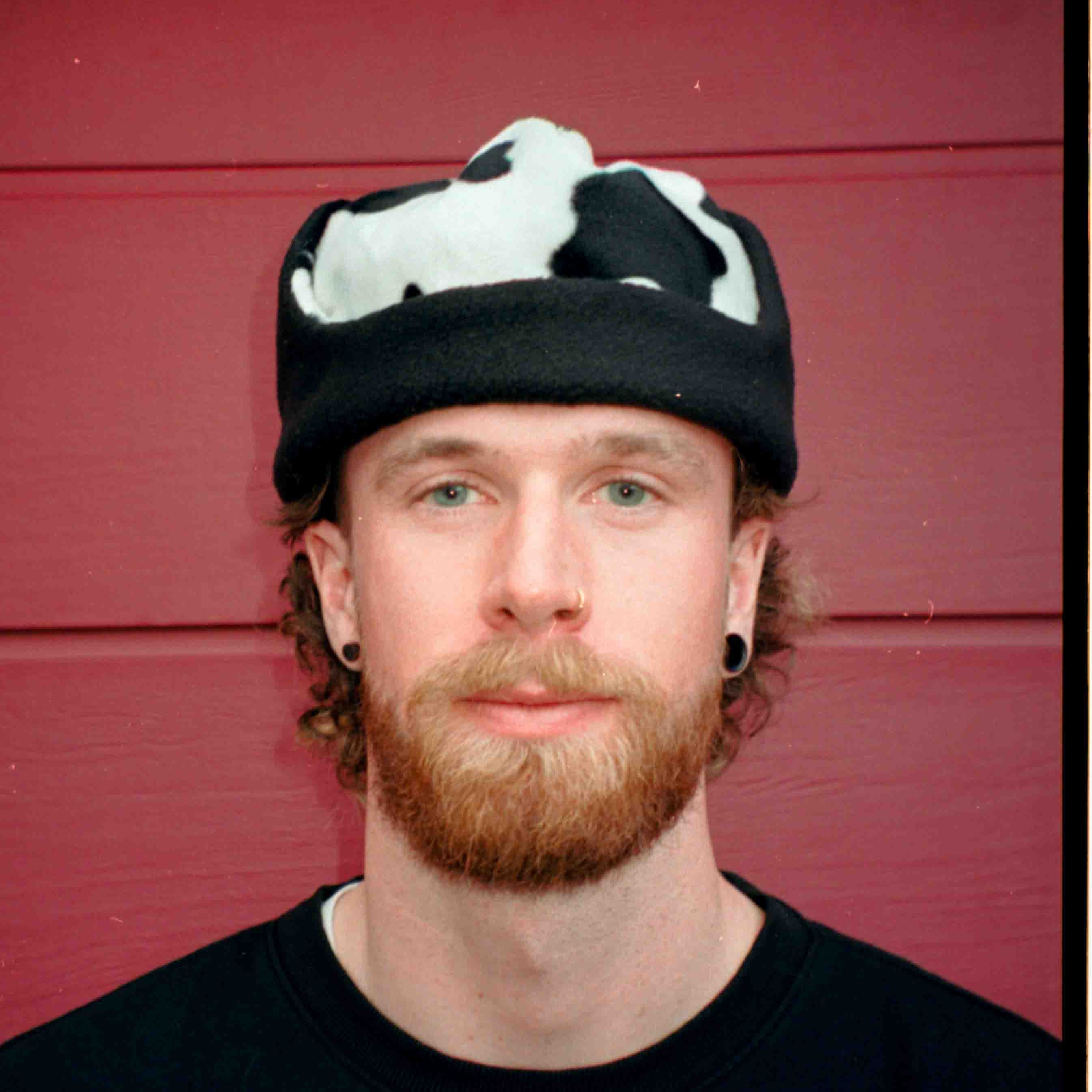 Man wearing a black and white cow print hat against a red wooden panel background