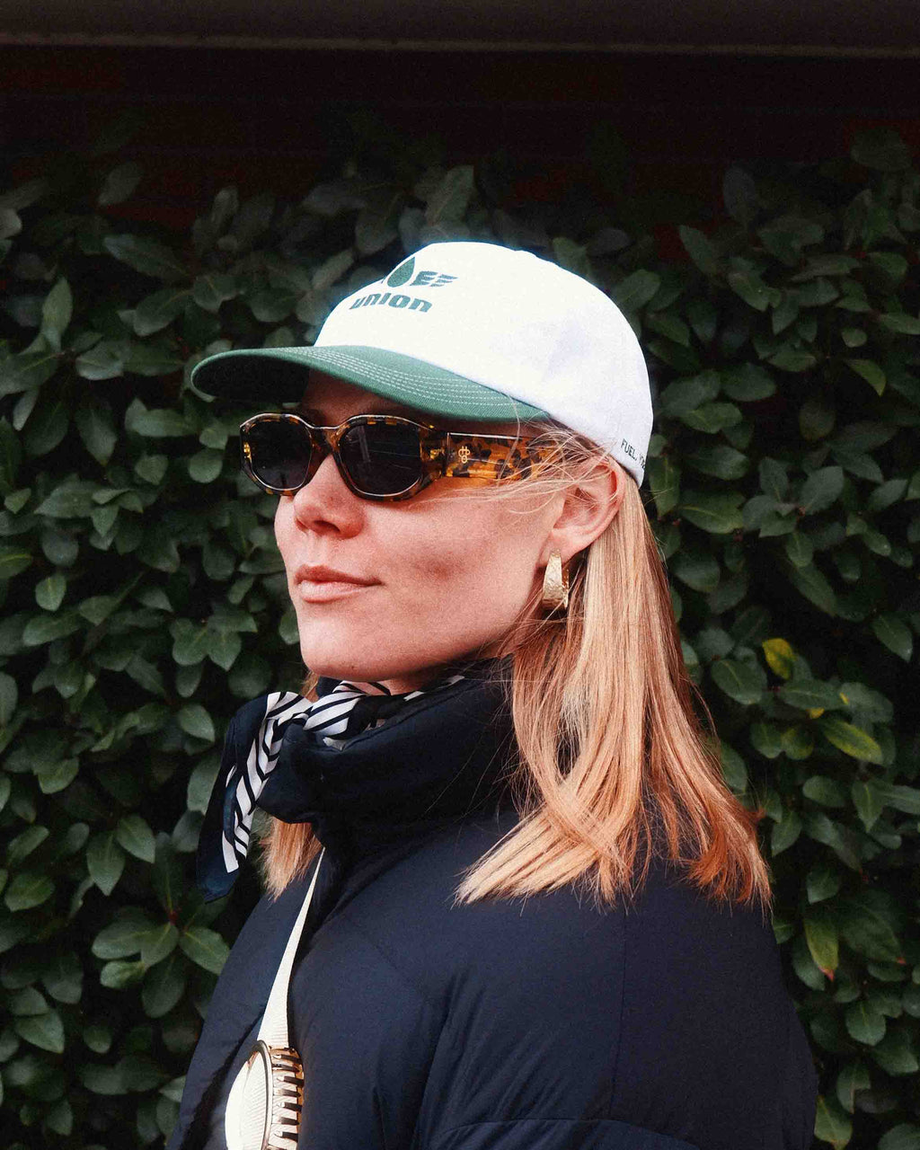 female model wearing Union.dsgn cap in city with a green backround