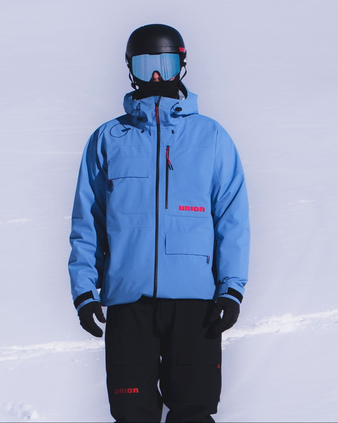 Person wearing a blue Union.dsgn ski jacket and black pants standing in the snow.